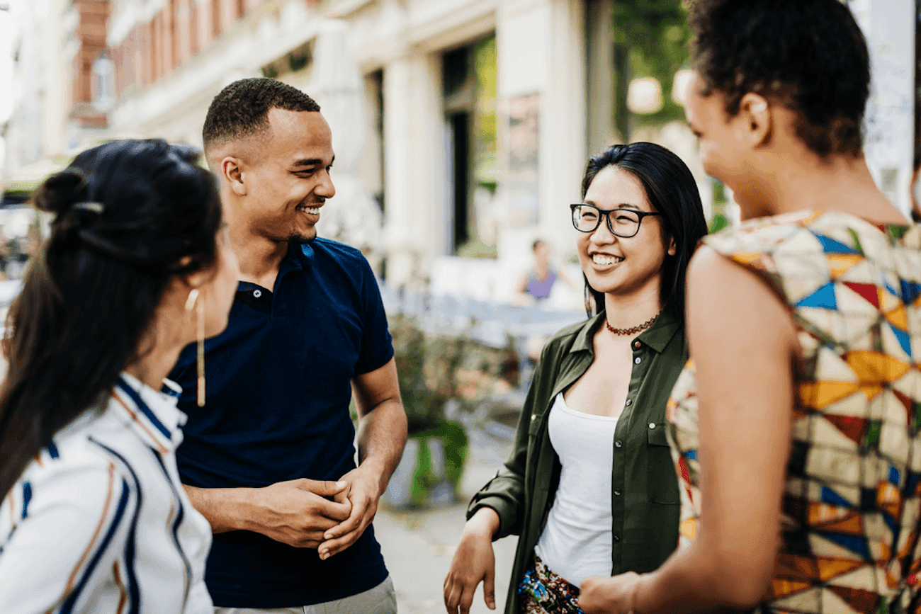 Four people standing on a city sidewalk smiling and talking.